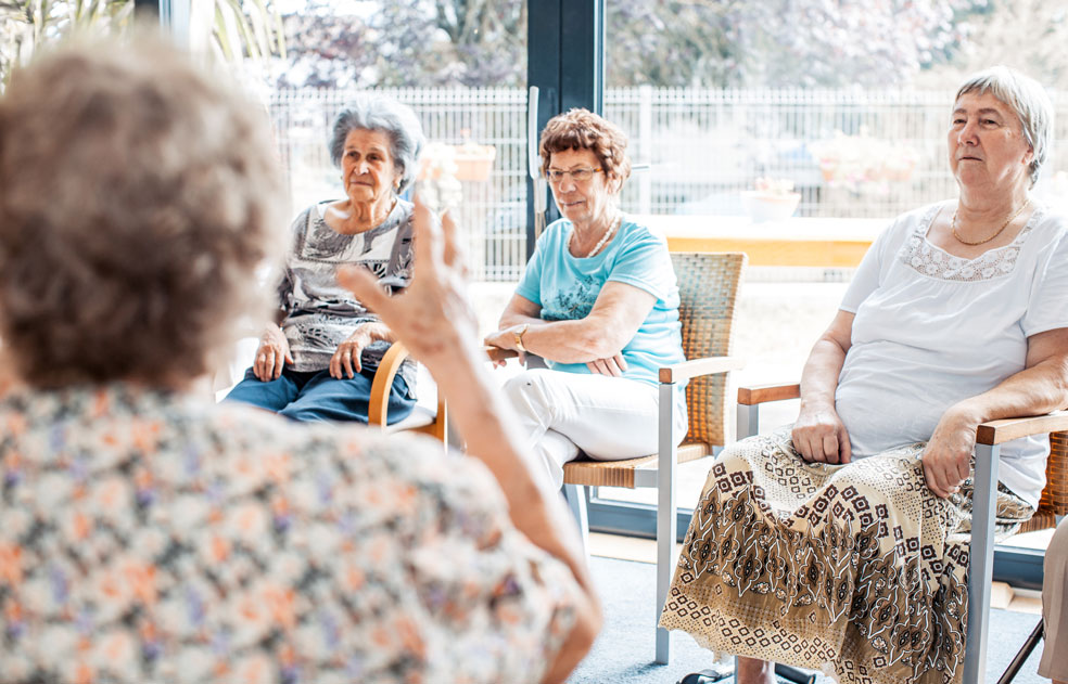 Group of four older women sitting in a circle while it appears one is speaking to the other three