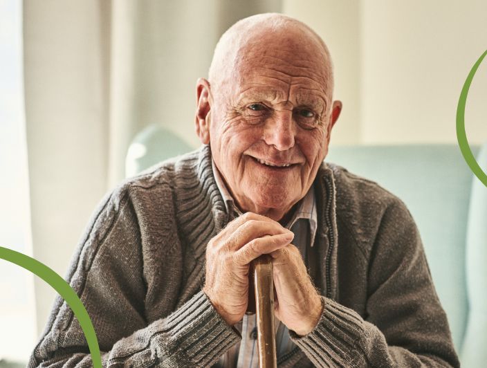 Older adult man seated in a comfty chair while smiling with a cane