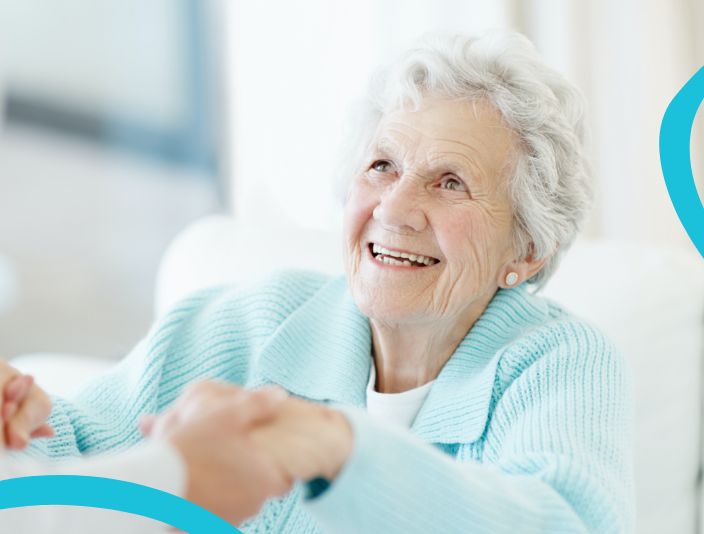 White haired woman in blue collared sweater smiling while being helped up by a pair of hands